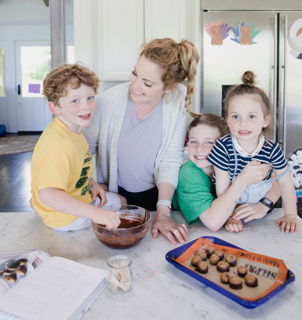 woman and children are the home kitchen counter smiling and making buckeyes together