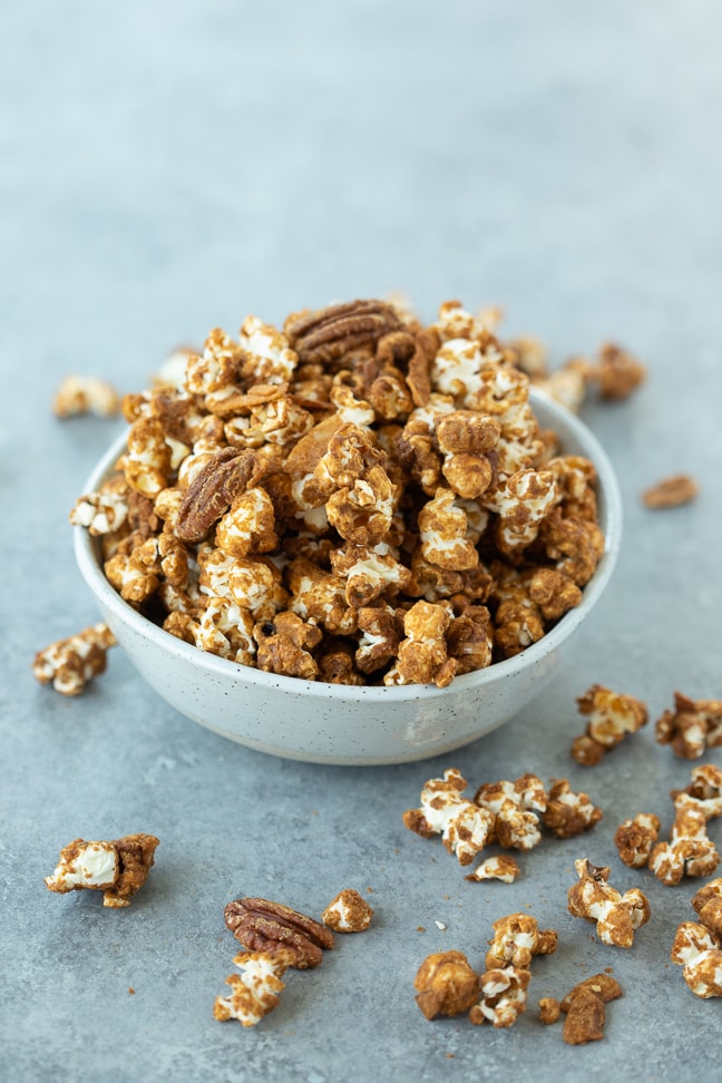 Gluten free caramel corn  with pecans and coconut in a white bowl on a gray surface