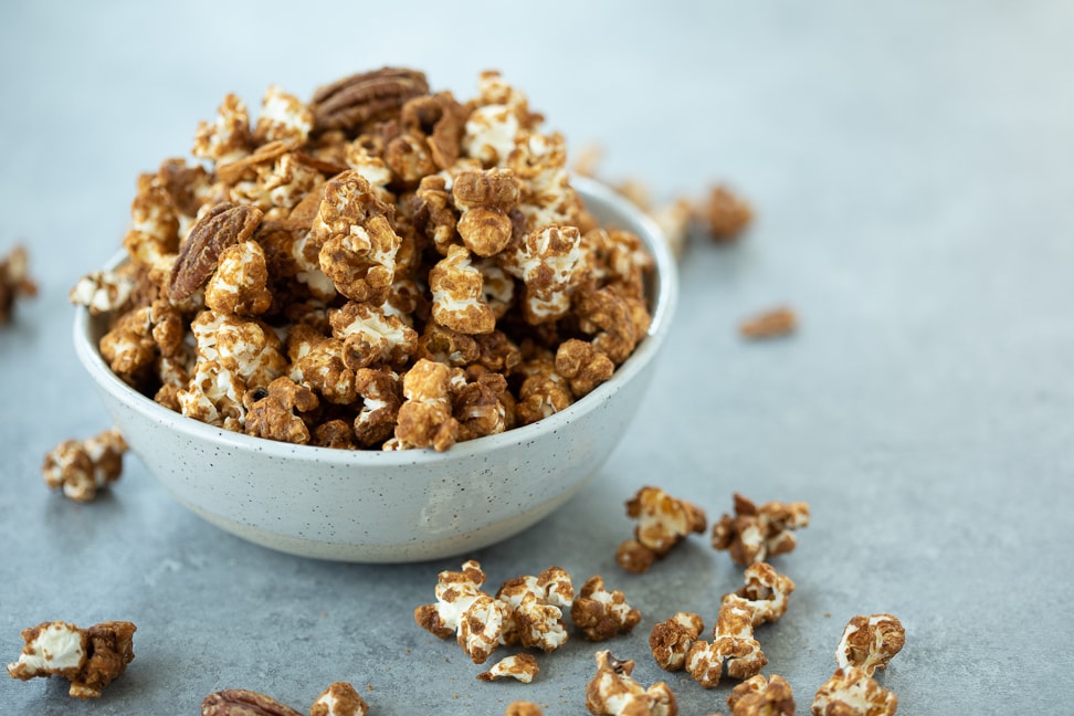 Gluten free caramel corn with pecans and coconut in a white bowl on a gray surface