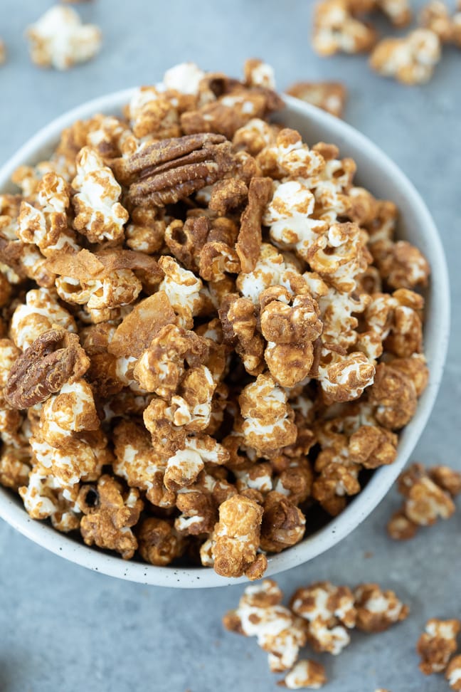 Gluten free caramel corn  with pecans and coconut in a white bowl on a gray surface