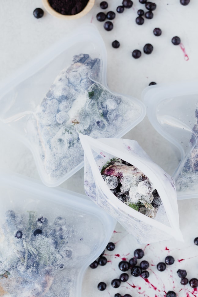 several small reusable plastic bags of frozen acai berries on a white counter with fresh acai berries