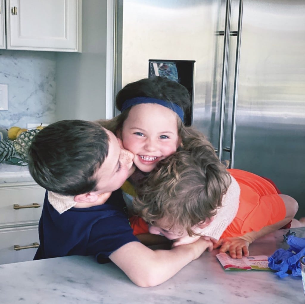 three children embrace each other and laugh while in home kitchen