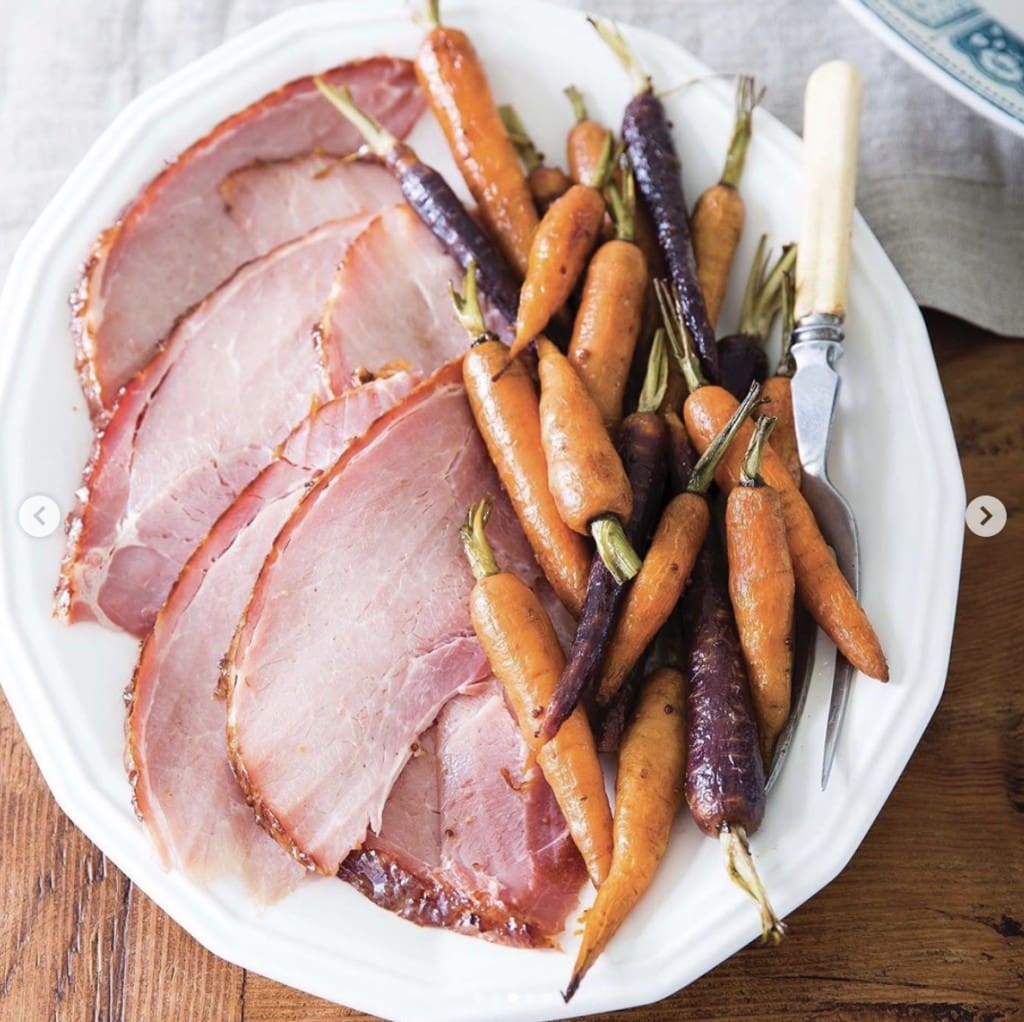white plate containing slices of ham and roasted carrots on a wooden table