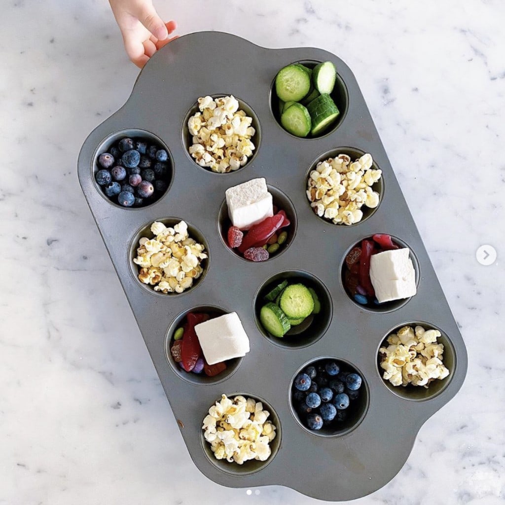 Tin Muffin pan filled with a variety of snacks such as cucumbers, marshmallows, blueberries and popcorn