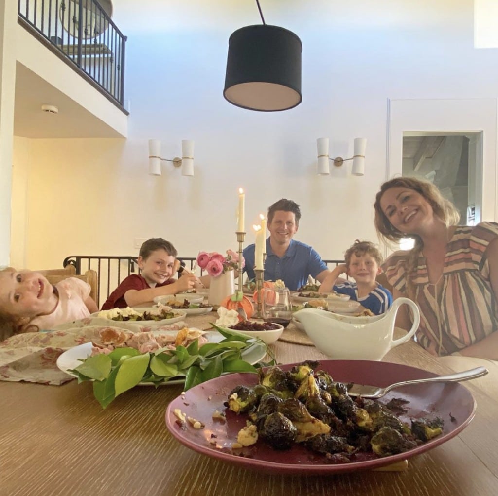 Family of adult male and female with three children sit gathered at a table that holds a Thanksgiving spread