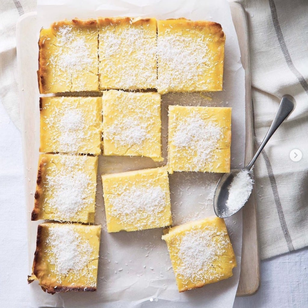 squares of lemon bars neatly arranged on a parchment paper placed on a wood cutting board