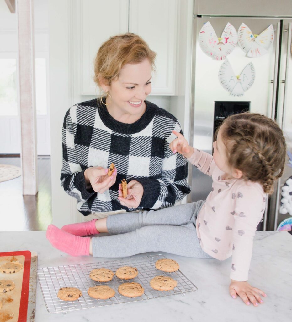 woman and young daughter hang in home kitchen bonding and smiling over freshly baked chocolate chip cookies