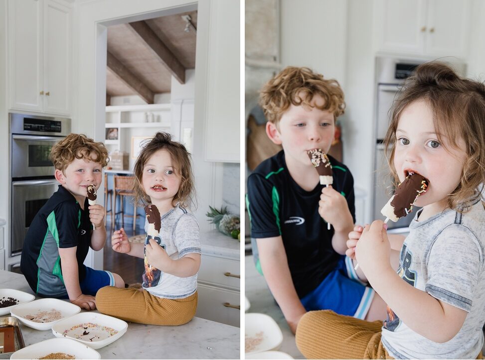 Children sit on home kitchen counter enjoying chocolate dipped bananas