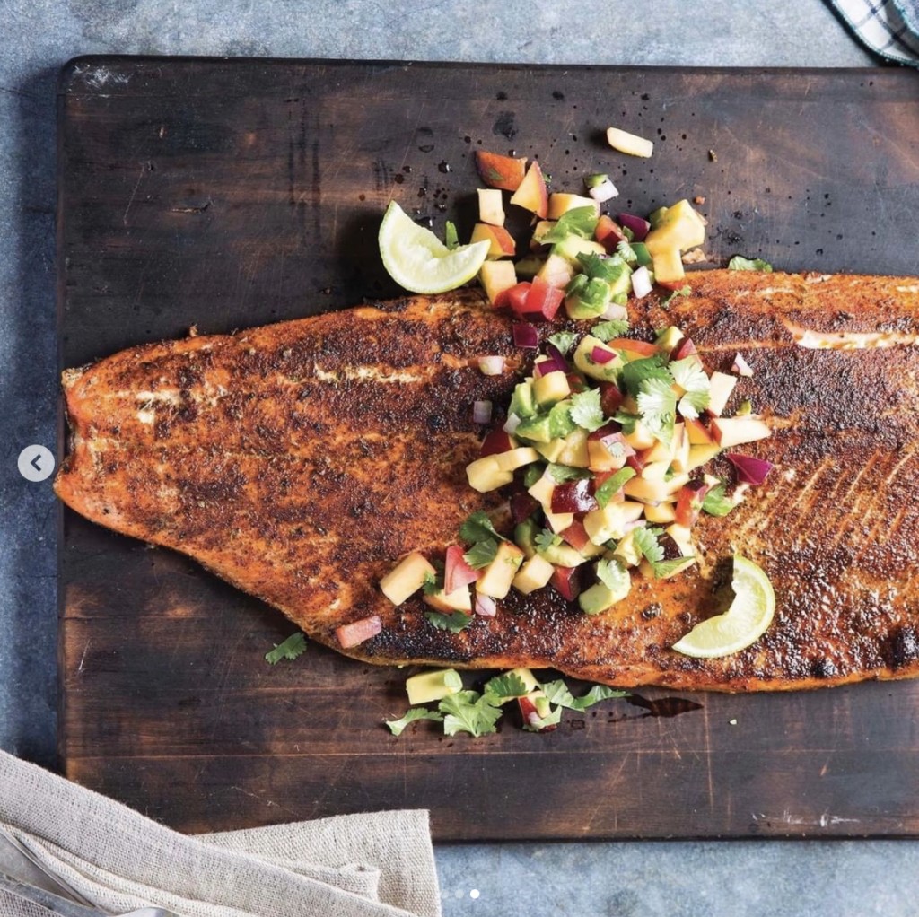 cooked blackened salmon topped with a mango avocado salsa lays on a dark wood cutting board