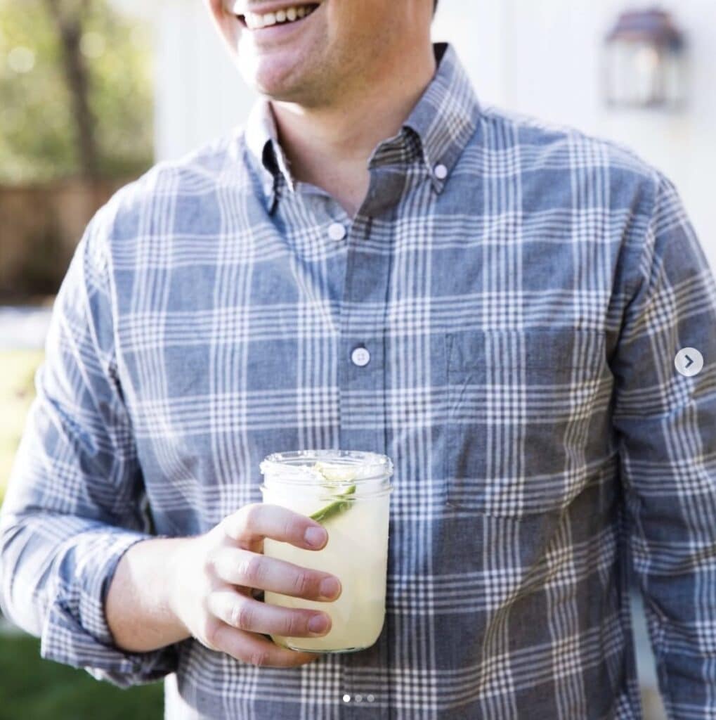 Man holds homemade margarita in right hand smiling off camera