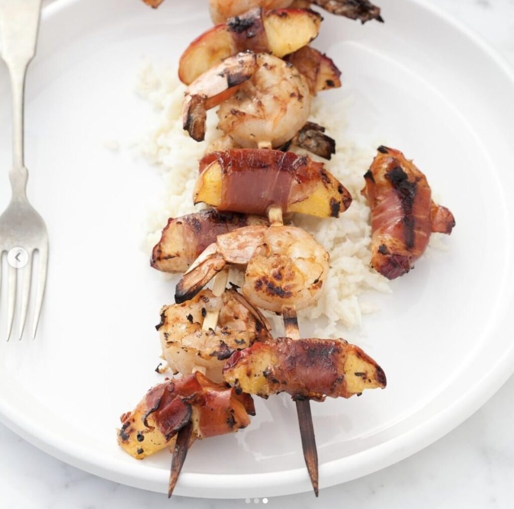 shrimp and Prosciutto wrapped peaches on wooden skewers served on a white plate over cauliflower rice