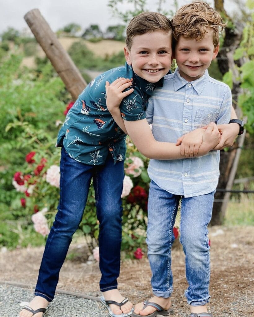 Two young male siblings embrace each other while smiling directly at the camera