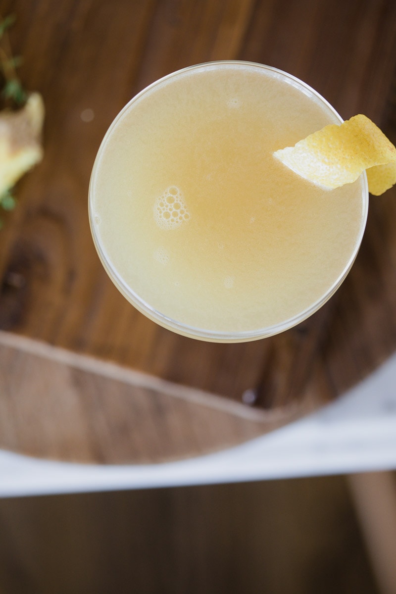 up close view of Ginger Thyme Tequila Sour cocktail garnished with lemon placed on a wooden cutting board