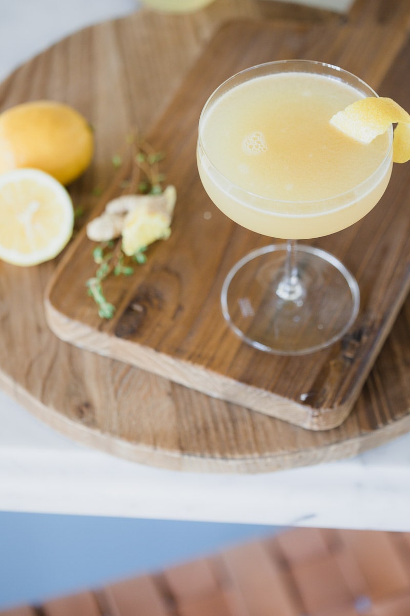 Ginger Thyme Tequila Sour cocktail garnished with lemon placed on wooden cutting boards