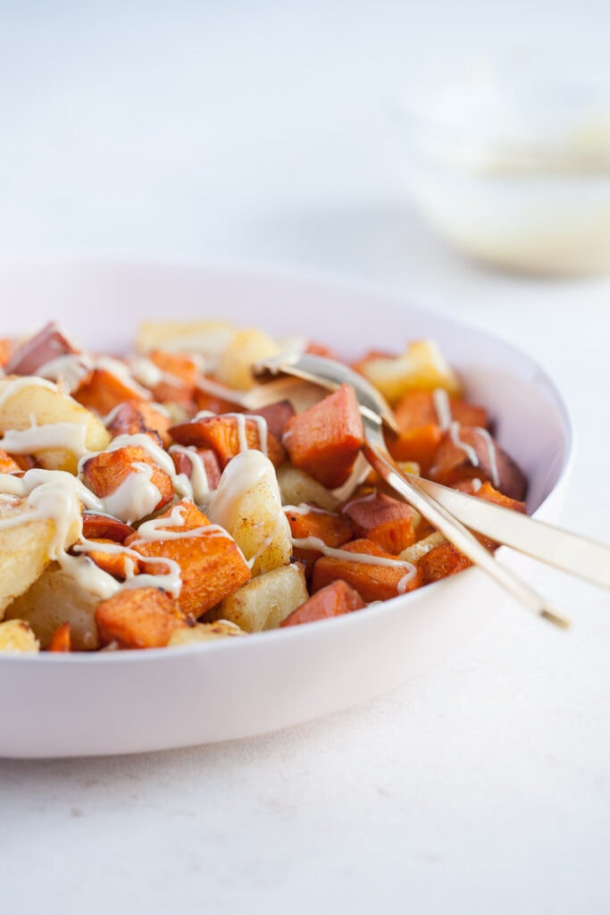 white bowl with gold colored spoon full of Roasted Pineapple and Sweet Potatoes with Cinnamon Cashew drizzle
