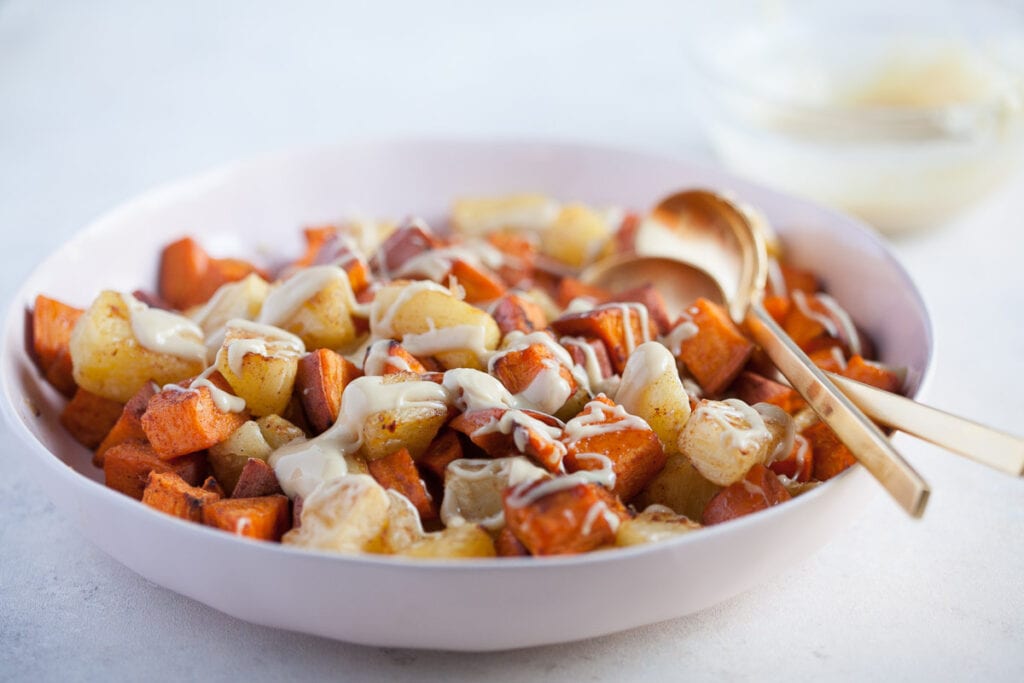 white bowl with gold colored spoon full of Roasted Pineapple and Sweet Potatoes with Cinnamon Cashew drizzle