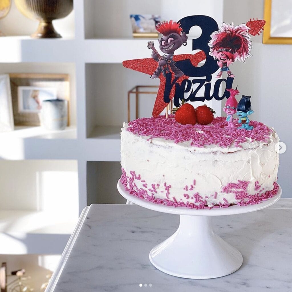 cake with sprinkles and Trolls movie decor with the number three on a white cake stand in home kitchen