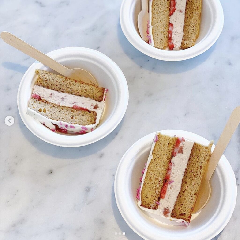 slices of strawberry ice cream with a vanilla cake serves in small white bowls with wooden spoons, all on a marble counter