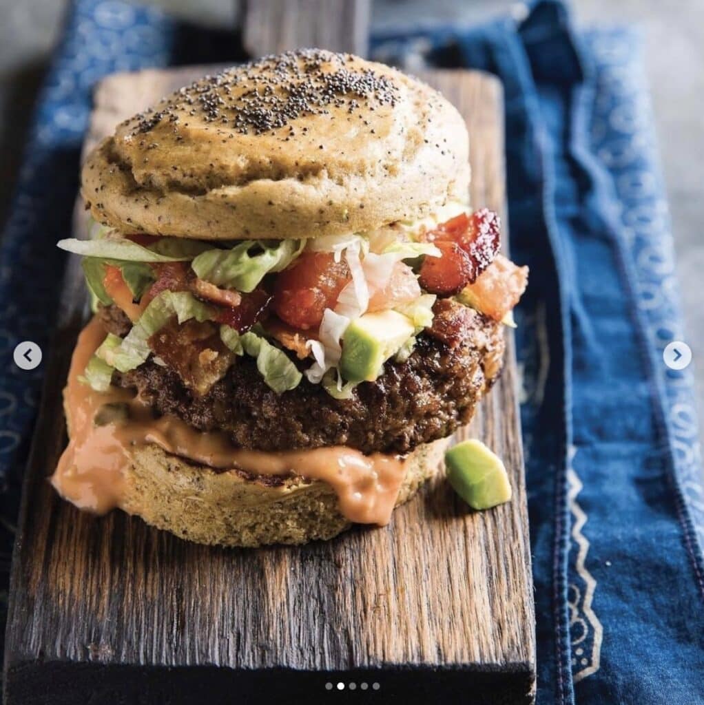 a burger with all the fixings set on a wooden board