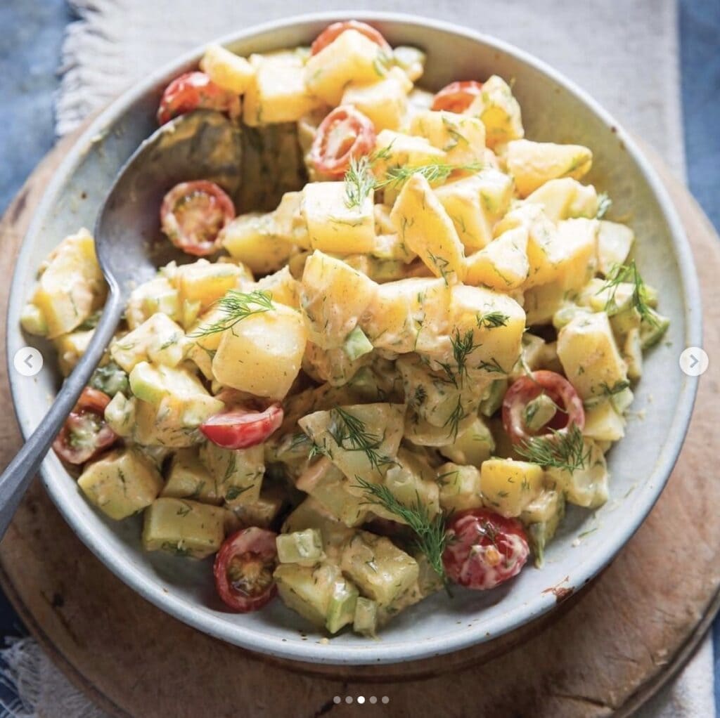 homemade potato salad with tomatoes and garnished with rosemary in a white bowl