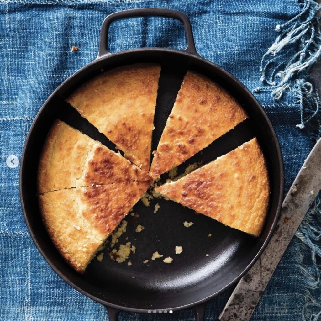 cornbread made in a skillet with several missing slices set on a jean tablecloth