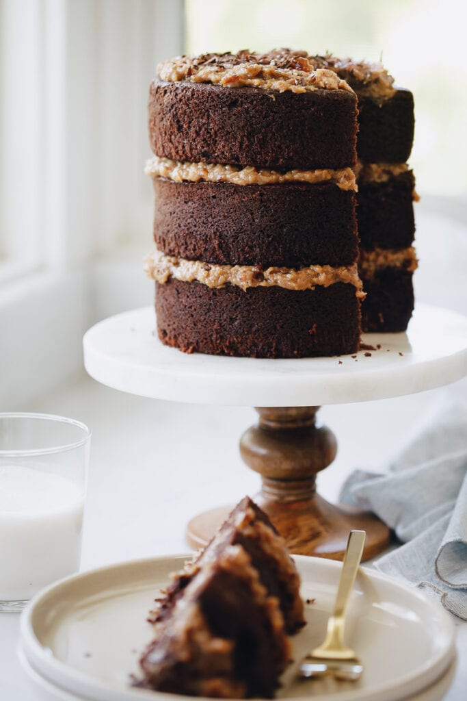 German Chocolate Cake resting on a cake platter and a slice of the cake is on a plate next to it 