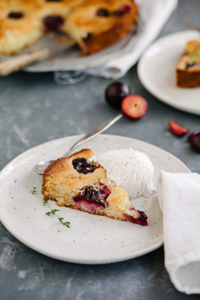 a slice of cardamom plum buckle served on white plate with a scoop of vanilla ice cream 