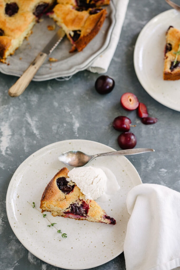 a slice of cardamom plum buckle served on white plate with a scoop of vanilla ice cream 