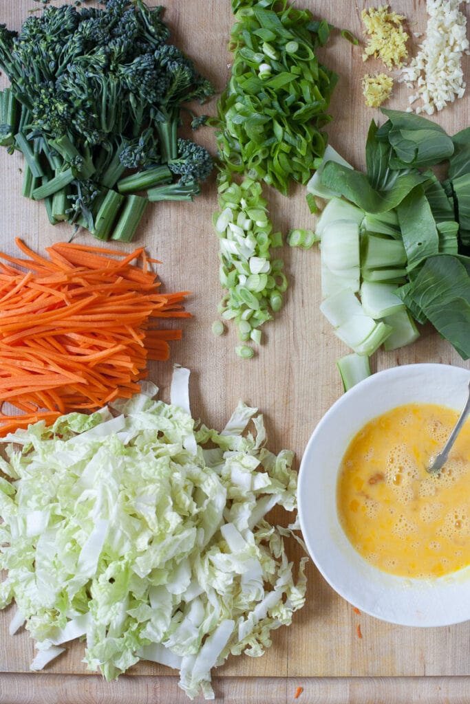 An assortment of vegetables and and beaten eggs in a white bowl placed on a wooden cutting board prior to being cooking to make Veggie Fried Rice