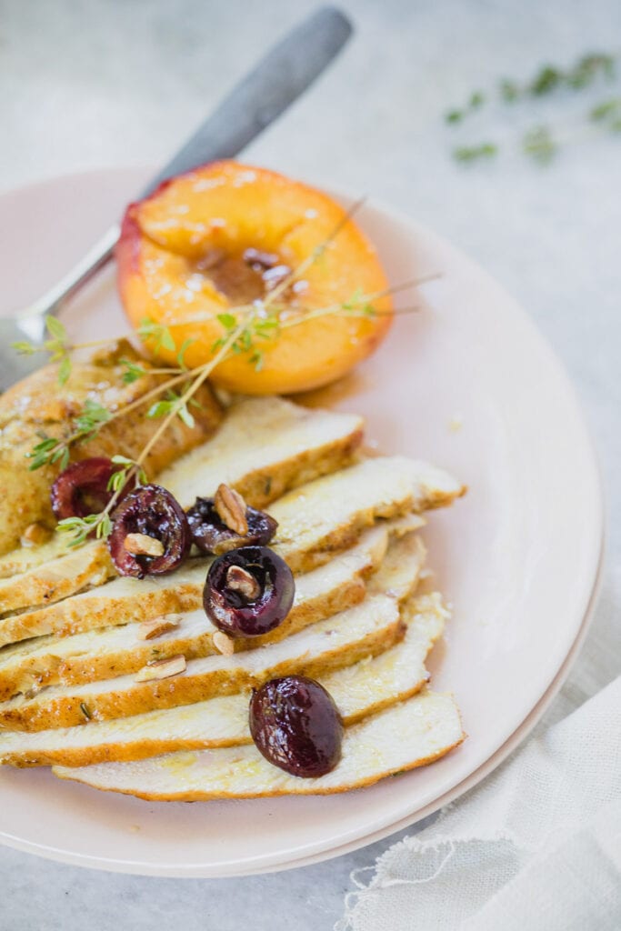 Sliced Spiced Roasted Chicken served on white plate with a peach on the side and cherries as a garnish