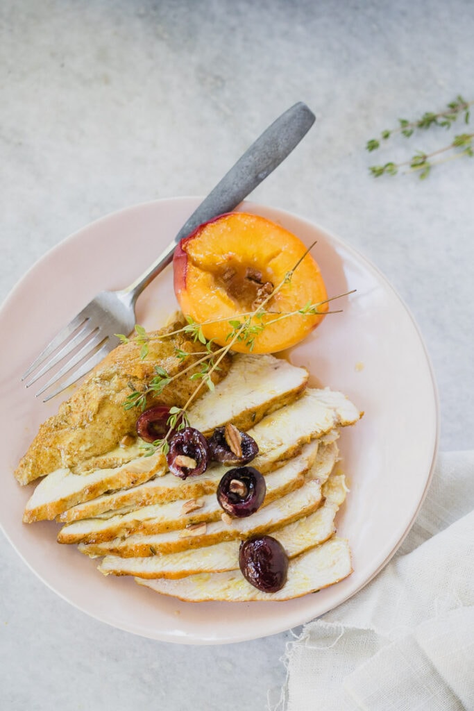 Sliced Spiced Roasted Chicken served on white plate with a peach on the side and cherries as a garnish