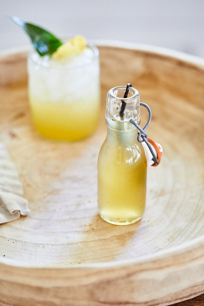 Vanilla Honey Simple Syrup on a wooden tray with a craft cocktail in the background