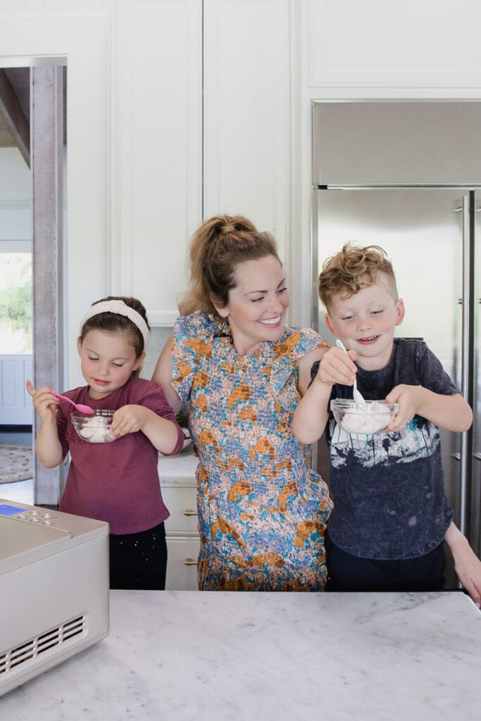 woman stands in kitchen smiling at son & daughter who eagerly dive into their bowls of dairy-free strawberry ice cream