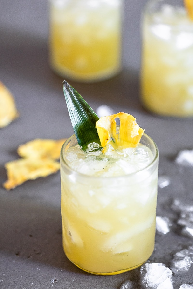 Vanilla Pineapple Margarita in a clear glass full of ice, garnished with a pineapple slice and leaf