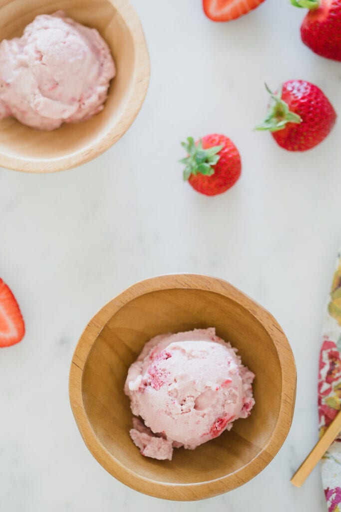 scoop of dairy-free strawberry ice cream in wooden bowl on white counter 