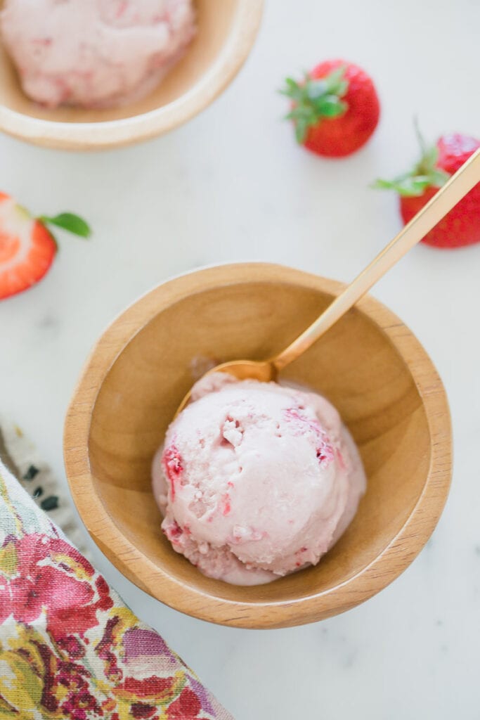 scoop of dairy-free strawberry ice cream in wooden bowl on white counter 