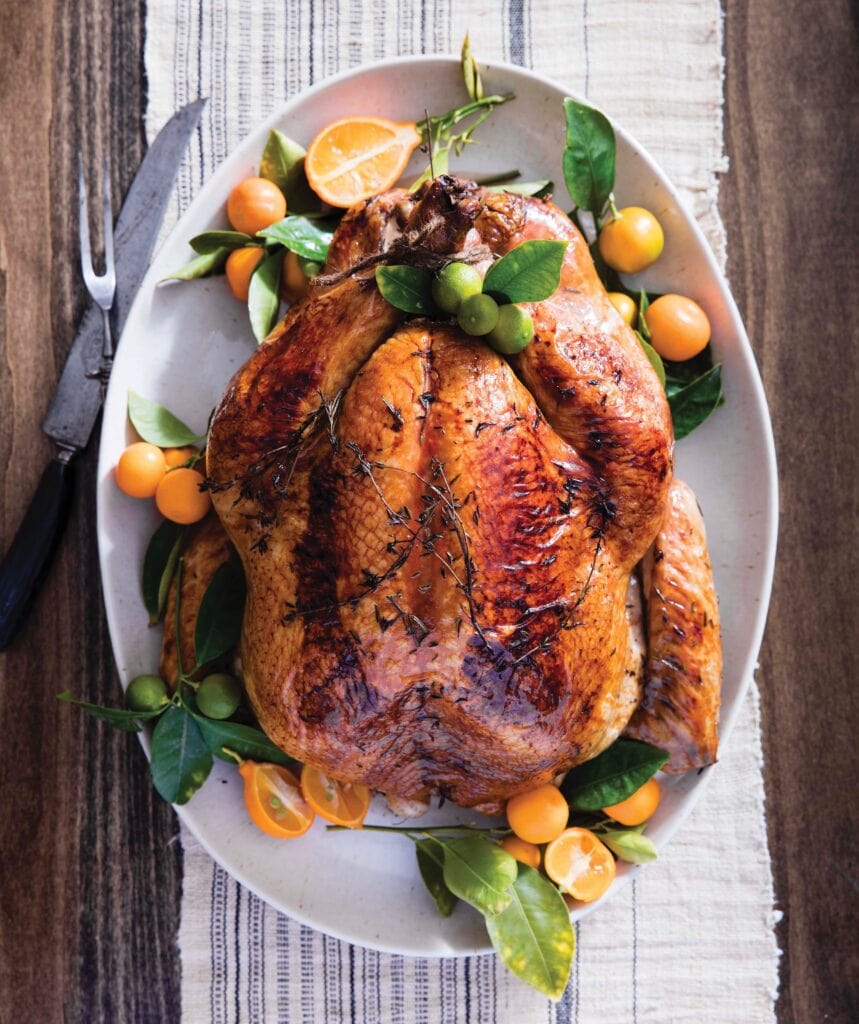 Thanksgiving Turkey fully cooked displayed on a white platter and adorned with small fruit & green leaves